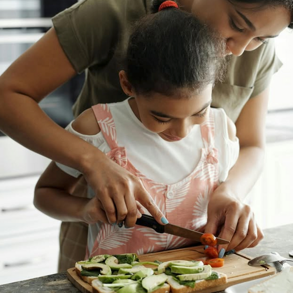 Woman and young girl preparing food together on a cutting board.
