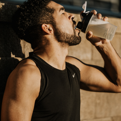 Man in black tank top drinking from a sports bottle outdoors
